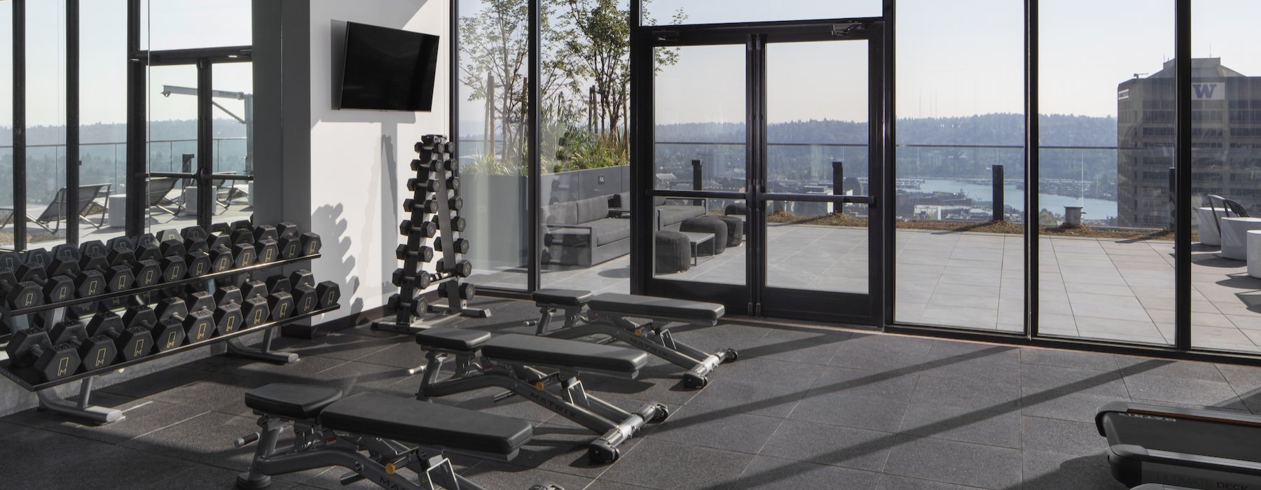 Fitness center with free weights and adjustable benches on a rooftop deck at The M Seattle apartments.